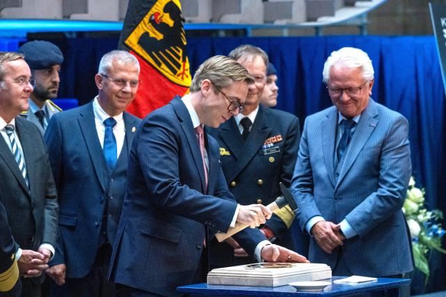 14 September 2026, Mecklenburg-Western Pomerania, Wolgast: Minister of State for Federal-State Relations at the Federal Chancellery Philipp Amthor (C) holds a hammer as the keel is laid for the third Class 424 fleet service boat at the Peene Shipyard. Standing next to him are Rheinmetall CEO Armin Papperger (R) and German Defense Minister Boris Pistorius (L). Photo: Stefan Sauer/dpa