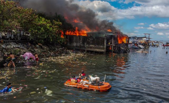 (241124) -- MANILA, Nov. 24, 2024 (Xinhua) -- Residents use a makeshift boat to evacuate with their pet dogs and their belongings as a fire engulfs a slum area in Manila, the Philippines on Nov. 24, 2024. (Xinhua/Rouelle Umali)