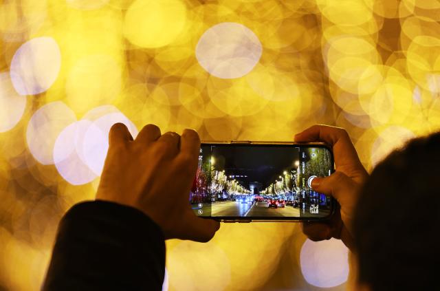 (241125) -- PARIS, Nov. 25, 2024 (Xinhua) -- A man takes photos at the Champs-Elysees lit by Christmas holiday lights in Paris, France, Nov. 24, 2024. The annual Christmas season lighting ceremony was held here on Sunday. The lights on the famed avenue will be turned on from 17:00 to midnight everyday and will last until the beginning of January 2024, with the exception of Dec. 24 and 31, when the lights will last all night long. (Xinhua/Gao Jing)