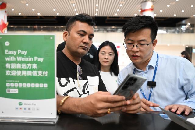 (241201) -- BEIJING, Dec. 1, 2024 (Xinhua) -- An Indian passenger (L) asks for information on a China's major mobile payment platform at Terminal 2 of Guangzhou Baiyun International Airport in Guangzhou, south China's Guangdong Province, April 3, 2024. (Xinhua/Deng Hua)