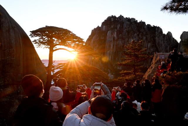 (250509) -- HUANGSHAN, May 9, 2025 (Xinhua) -- Tourists watch the sunrise at the Guest-Greeting Pine, an iconic landmark of Huangshan Mountain, in east China's Anhui Province, on Jan. 1, 2025. Huangshan Mountain is a listed UNESCO World Cultural and Natural Heritage Site, which has attracted a large number of tourists.
  To minimize the impact of visitors on its vegetation growth, the Huangshan Scenic Area rotates days off for its major scenic spots, as a special arrangement for ecological protection.
   The Tiandu Peak, one of the most popular sites in the Huangshan scenic area, ended its more than five-year "vacation" and resumed opening to the public on May 20, 2024. While the Lianhua Peak, the highest peak of Huangshan Mountain, has been so far closed for more than a year. (Xinhua/Huang Bohan)