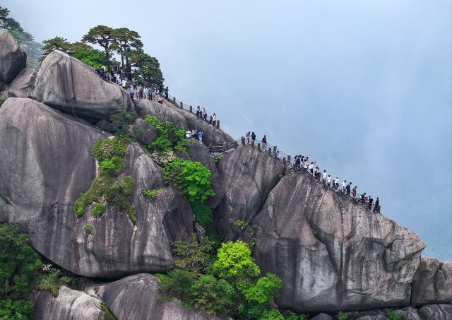 (250509) -- HUANGSHAN, May 9, 2025 (Xinhua) -- An aerial drone photo taken on May 20, 2024 shows tourists visiting the Tiandu Peak as it resumed opening in Huangshan Scenic Area in east China's Anhui Province. Huangshan Mountain is a listed UNESCO World Cultural and Natural Heritage Site, which has attracted a large number of tourists.
  To minimize the impact of visitors on its vegetation growth, the Huangshan Scenic Area rotates days off for its major scenic spots, as a special arrangement for ecological protection.
   The Tiandu Peak, one of the most popular sites in the Huangshan scenic area, ended its more than five-year "vacation" and resumed opening to the public on May 20, 2024. While the Lianhua Peak, the highest peak of Huangshan Mountain, has been so far closed for more than a year. (Photo by Shi Yalei/Xinhua)