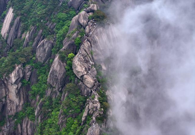 (250509) -- HUANGSHAN, May 9, 2025 (Xinhua) -- An aerial drone photo taken on May 20, 2024 shows tourists visiting the Tiandu Peak as it resumed opening in Huangshan Scenic Area in east China's Anhui Province. Huangshan Mountain is a listed UNESCO World Cultural and Natural Heritage Site, which has attracted a large number of tourists.
  To minimize the impact of visitors on its vegetation growth, the Huangshan Scenic Area rotates days off for its major scenic spots, as a special arrangement for ecological protection.
   The Tiandu Peak, one of the most popular sites in the Huangshan scenic area, ended its more than five-year "vacation" and resumed opening to the public on May 20, 2024. While the Lianhua Peak, the highest peak of Huangshan Mountain, has been so far closed for more than a year. (Photo by Shi Yalei/Xinhua)