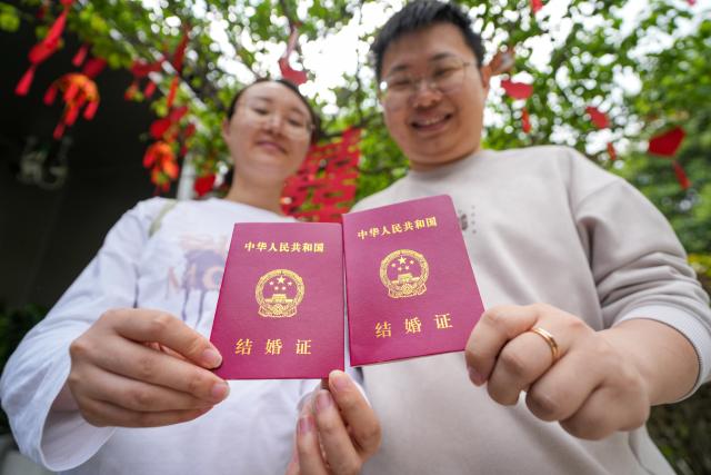 (250511) -- BEIJING, May 11, 2025 (Xinhua) -- A couple poses for photos with their marriage certificates at a marriage registration office in the Xuanwu Lake Park in Nanjing, east China's Jiangsu Province, May 10, 2025. (Xinhua/Li Bo)