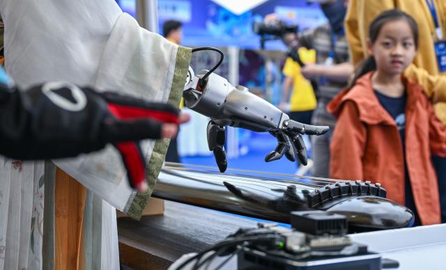 (250602) -- WUHAN, June 2, 2025 (Xinhua) -- Visitors watch a robot playing Guqin, a plucked seven-string traditional Chinese musical instrument, during the world robot carnival in Wuhan, central China's Hubei Province, June 2, 2025. The event kicked off here on Monday, featuring nearly 100 robots including pet robots, make-up robots, robotics band, etc. People interacted with the robots to experience the charm of technology-empowered life. (Xinhua/Du Zixuan)