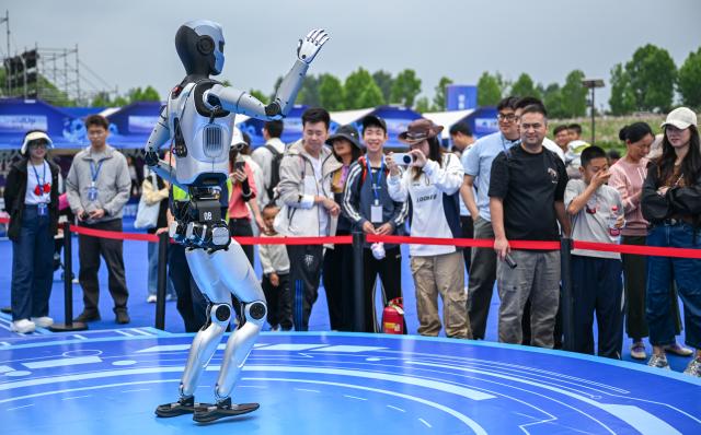 (250602) -- WUHAN, June 2, 2025 (Xinhua) -- Visitors watch a robot performing during the world robot carnival in Wuhan, central China's Hubei Province, June 2, 2025. The event kicked off here on Monday, featuring nearly 100 robots including pet robots, make-up robots, robotics band, etc. People interacted with the robots to experience the charm of technology-empowered life. (Xinhua/Du Zixuan)
