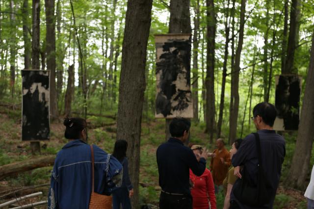 (250630) -- LENOX (U.S.), June 30, 2025 (Xinhua) -- People visit an outdoor exhibition "Solar Terms: Contemporary Ink Art Event" in Lenox, Massachusetts, the United States, on June 28, 2025. In a wooded corner of Eastover Estate & Eco-Village, a dozen tall scrolls, roughly a meter wide and three meters high, sway quietly in summer breeze, having been visibly transformed by rain, snow, sunlight and time since they were installed one year ago. The scrolls were painted on rice paper, affixed to durable non-woven fabric, and then framed and suspended between trees in the forest of the U.S. state of Massachusetts. (Xinhua/Zhang Fengguo) TO GO WITH Feature: Chinese artists test nature's hand in U.S. Massachusetts forest