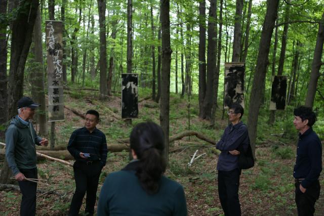 (250630) -- LENOX (U.S.), June 30, 2025 (Xinhua) -- Curators Zhang Pingjie (2nd R) and Xu Yufu (1st L), and Chinese contemporary ink painter Lan Zhenghui (1st R) join a discussion with visitors during an outdoor exhibition "Solar Terms: Contemporary Ink Art Event" in Lenox, Massachusetts, the United States, on June 28, 2025. In a wooded corner of Eastover Estate & Eco-Village, a dozen tall scrolls, roughly a meter wide and three meters high, sway quietly in summer breeze, having been visibly transformed by rain, snow, sunlight and time since they were installed one year ago. The scrolls were painted on rice paper, affixed to durable non-woven fabric, and then framed and suspended between trees in the forest of the U.S. state of Massachusetts. (Xinhua/Zhang Fengguo) TO GO WITH Feature: Chinese artists test nature's hand in U.S. Massachusetts forest