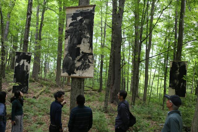 (250630) -- LENOX (U.S.), June 30, 2025 (Xinhua) -- Chinese painter Lan Zhenghui (3rd L) introduces his work during an outdoor exhibition "Solar Terms: Contemporary Ink Art Event" in Lenox, Massachusetts, the United States, on June 28, 2025. In a wooded corner of Eastover Estate & Eco-Village, a dozen tall scrolls, roughly a meter wide and three meters high, sway quietly in summer breeze, having been visibly transformed by rain, snow, sunlight and time since they were installed one year ago. The scrolls were painted on rice paper, affixed to durable non-woven fabric, and then framed and suspended between trees in the forest of the U.S. state of Massachusetts. (Xinhua/Zhang Fengguo) TO GO WITH Feature: Chinese artists test nature's hand in U.S. Massachusetts forest