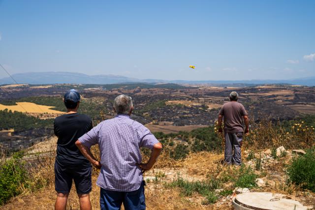(250702) -- LLEIDA, July 2, 2025 (Xinhua) -- Local residents watch a firefighting plane in Lleida province, Spain, July 2, 2025. Two farmers were killed in a wildfire that burned through 5,000 hectares in the La Segarra district of Lleida province, north-east Spain, on Tuesday, according to local emergency services. (Photo by Joan Gosa/Xinhua)