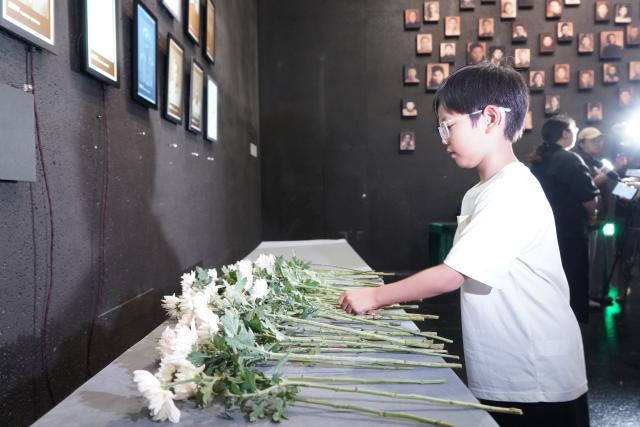 (250703) -- NANJING, July 3, 2025 (Xinhua) -- Sun Guoting, descendant of the Nanjing Massacre survivor Liu Guixiang, lays a flower during a "lights out" ceremony held at the Memorial Hall of the Victims in Nanjing Massacre by Japanese Invaders in Nanjing, east China's Jiangsu Province, July 2, 2025. A "lights out" ceremony for two survivors of the Nanjing Massacre who passed away this year was held here on Wednesday. On a photo wall featuring survivors of the Nanjing Massacre, the lightboxes of Liu Guixiang and Xie Guiying were dimmed off, and their colored photos then turned to black and white.
   With the passing away of Liu and Xie earlier this year, the number of living registered survivors has decreased to 26. (Photo by Liu Zhenrui/Xinhua)
