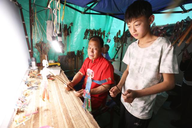 (250703) -- TONGWEI, July 3, 2025 (Xinhua) -- A student plays a shadow puppet under the guide of Liu Mancang in Changjiahe Town of Tongwei County, northwest China's Gansu Province, July 1, 2025. After harvesting his own wheat, Liu Mancang, an inheritor of the national intangible cultural heritage project Tongwei Shadow Puppetry, began traveling through the village to perform shadow play for his fellow villagers in Changjiahe Town, Tongwei County, making the most of his leisure time during the farming off season.
   Tongwei Shadow Puppetry is widely spread across Dingxi, Tianshui and Longnan in Gansu Province. It is a folk drama in which animal skins or cardboard are made into silhouettes to perform stories. 
   Liu, now 60, began to learn shadow puppetry from his grandfather at the age of 12. After decades of study, he has mastered the skills of shadow puppetry proficiently and collected and sorted out over a hundred shadow puppetry scripts. In 2018, he was recognized as an inheritor of Tongwei Shadow Puppetry.
   Liu has visited and studied in provinces like Shaanxi, Henan and Guangdong. While improving his own skills, he also promoted Tongwei Shadow Puppetry through voluntary performances in schools, hoping that this ancient folk art would shine with new luster. (Photo by Wang Kexian/Xinhua)