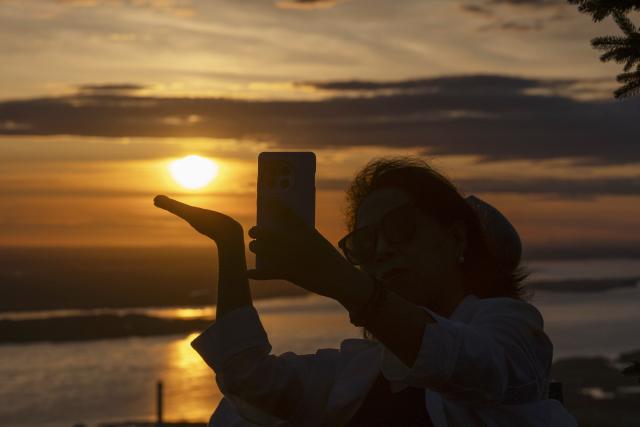 (250704) -- BEIJING, July 4, 2025 (Xinhua) -- A tourist takes photos with the rising sun at Dongji Pavilion in Fuyuan City, northeast China's Heilongjiang Province, July 4, 2025. The Earth passed the aphelion on July 4, which is the time of year when the Earth is farthest from the sun, and the apparent diameter of the sun is the smallest in the year. (Xinhua/Zhang Tao)