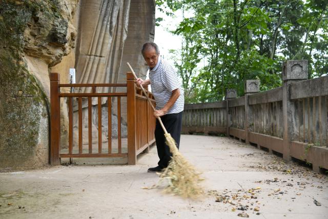 (250705) -- ZIYANG, July 5, 2025 (Xinhua) -- Zeng Xiangyu cleans the fallen leaves at Mingshan Temple in Shiyang Town of Ziyang City, southwest China's Sichuan Province, June 14, 2025. On top of Hutou Mountain in Shiyang Town of Ziyang City, a 76-year-old man named Zeng Xiangyu is a familiar sight to locals. Accompanied by his dog, he patrols the circular path around Mingshan Temple, meticulously inspecting each stone carving.
   Dating back to the Tang Dynasty (618-907), Mingshan Temple houses over 60 statues inside 13 caves. Most of these magnificent works of artistry were chiseled during the Song Dynasty (960-1127).
   In the 1980s, Zeng first came to the mountain with his uncle for temple renovation work. Since then, he has devoted his life to safeguarding these relics. When Mingshan Temple was listed as a national key cultural relics protection site in 2006, Zeng formally became its on-site cultural heritage administrator.
   Today, as visitors flock to Mingshan Temple, Zeng occasionally steps into a part-time role as a guide, narrating centuries-old tales. He has expressed that he wishes to protect these sculptural treasures passed down from ancestors to future generations. (Xinhua/Xu Bingjie)