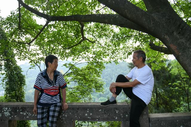 (250705) -- ZIYANG, July 5, 2025 (Xinhua) -- Zeng Xiangyu talks with his wife near Mingshan Temple in Shiyang Town of Ziyang City, southwest China's Sichuan Province, June 14, 2025. On top of Hutou Mountain in Shiyang Town of Ziyang City, a 76-year-old man named Zeng Xiangyu is a familiar sight to locals. Accompanied by his dog, he patrols the circular path around Mingshan Temple, meticulously inspecting each stone carving.
   Dating back to the Tang Dynasty (618-907), Mingshan Temple houses over 60 statues inside 13 caves. Most of these magnificent works of artistry were chiseled during the Song Dynasty (960-1127).
   In the 1980s, Zeng first came to the mountain with his uncle for temple renovation work. Since then, he has devoted his life to safeguarding these relics. When Mingshan Temple was listed as a national key cultural relics protection site in 2006, Zeng formally became its on-site cultural heritage administrator.
   Today, as visitors flock to Mingshan Temple, Zeng occasionally steps into a part-time role as a guide, narrating centuries-old tales. He has expressed that he wishes to protect these sculptural treasures passed down from ancestors to future generations. (Xinhua/Xu Bingjie)