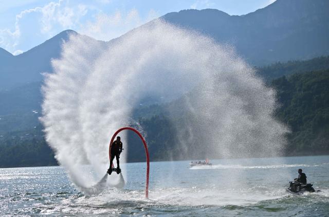 (250708) -- ENSHI, July 8, 2025 (Xinhua) -- A staff member of the aquatic sports center performs a "Water Flyer" show in Jianshi County, Enshi Tujia and Miao Autonomous Prefecture, central China's Hubei Province, July 7, 2025. Enshi is a well-known summer travel destination in central China. Tapping diverse ecological resources, such as unique karst landforms, pleasant alpine climate, and dense primeval forests, the local authorities have actively developed summer tourism, and meticulously created diversified tourism products, like exploring canyon and cave, rafting on Qingjiang River and experiencing the culture of Tujia ethnic group. (Photo by Song Wen/Xinhua)