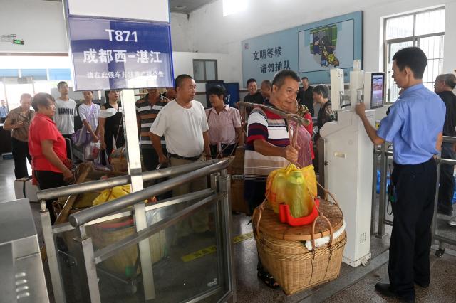 (250711) -- NANNING, July 11, 2025 (Xinhua) -- Fruit farmers carrying fruits and daily necessities check in at Hechun Station of Litang-Zhanjiang Railway, south China's Guangdong Province, July 10, 2025. The green-painted trains running on the Litang-Zhanjiang Railway offer a very cost-effective ride to fruit farmers. The relatively slow trains stop at more stations compared with the speedy bullet trains. To provide convenience for farmers to sell their fruits, the railway department has set up special waiting areas at the stations, and the railway staff often offer a helping hand to them who are carrying heavy baskets. (Xinhua/Lu Boan)