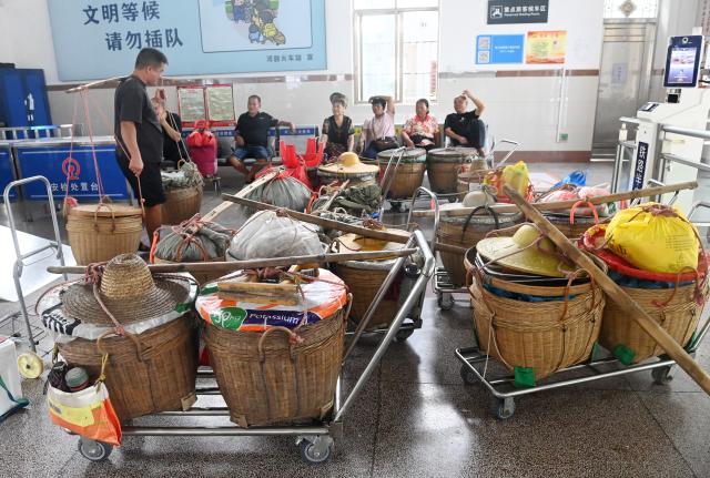 (250711) -- NANNING, July 11, 2025 (Xinhua) -- Fruit farmers, putting their fruit baskets in the waiting hall, wait for check-in at Hechun Station of Litang-Zhanjiang Railway, south China's Guangdong Province, July 10, 2025. The green-painted trains running on the Litang-Zhanjiang Railway offer a very cost-effective ride to fruit farmers. The relatively slow trains stop at more stations compared with the speedy bullet trains. To provide convenience for farmers to sell their fruits, the railway department has set up special waiting areas at the stations, and the railway staff often offer a helping hand to them who are carrying heavy baskets. (Xinhua/Lu Boan)