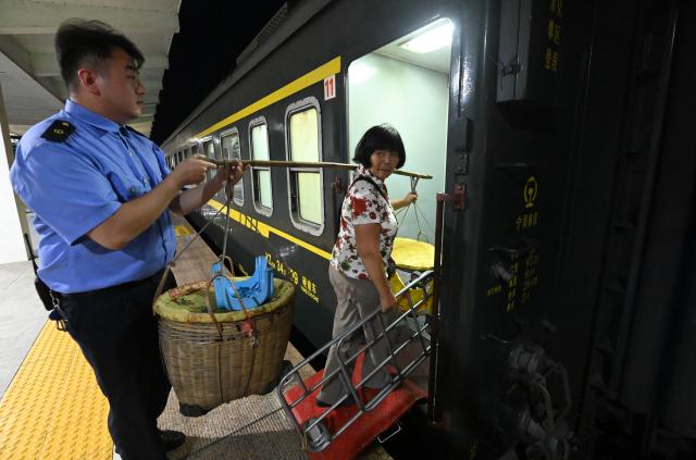 (250711) -- NANNING, July 11, 2025 (Xinhua) -- A railway attendant (L) helps a fruit farmer carrying her baskets onto a train at Luchuan Station of Litang-Zhanjiang Railway, south China's Guangxi Zhuang Autonomous Region, July 9, 2025. The green-painted trains running on the Litang-Zhanjiang Railway offer a very cost-effective ride to fruit farmers. The relatively slow trains stop at more stations compared with the speedy bullet trains. To provide convenience for farmers to sell their fruits, the railway department has set up special waiting areas at the stations, and the railway staff often offer a helping hand to them who are carrying heavy baskets. (Xinhua/Lu Boan)