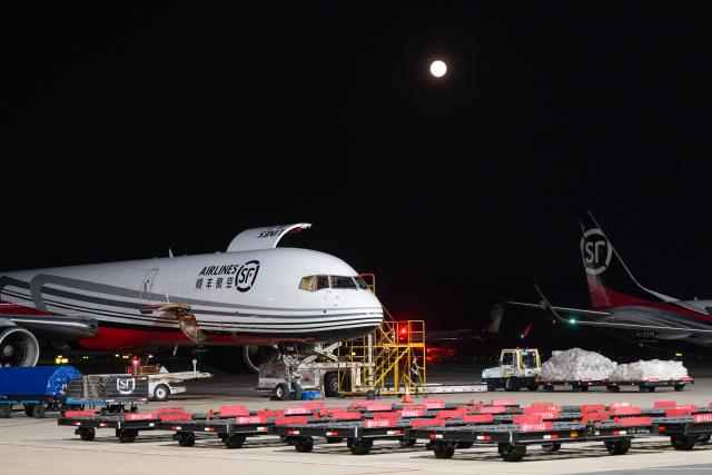 (250712) -- EZHOU, July 12, 2025 (Xinhua) -- Workers transfer goods at the apron of Ezhou Huahu International Airport in Ezhou, central China's Hubei Province, July 11, 2025. Brightly lit during the night, Ezhou Huahu International Airport, China's first cargo-focused airport, is kept awake handling cargo from home and abroad. Starting operation in July 2022, the airport, owning a 750,000-square meter cargo transfer center with parcel sorting lines adding up to 52 kilometers, is now running 59 domestic cargo routes in addition to 45 international routes. (Xinhua/Xiao Yijiu)