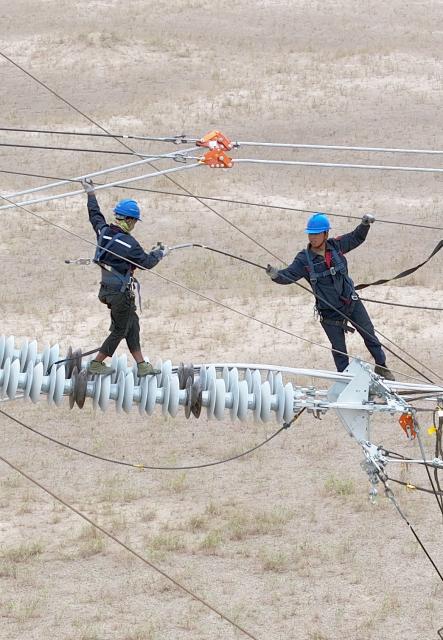 (250713) -- MINFENG, July 13, 2025 (Xinhua) -- A drone photo shows Chen Lin (R) operating on a power transmission tower at a construction site in Minfeng County, of Hotan Prefecture, northwest China's Xinjiang Uygur Autonomous Region, July 12, 2025. China has finished construction of a 4,197-km extra-high voltage power transmission loop around the Tarim Basin, home to the country's largest desert, marking a major infrastructure milestone in southern Xinjiang Uygur Autonomous Region.
   The final section of the 750-kilovolt (kV) loop, now the country's largest of its kind, was connected on Sunday, capping a 15-year project involving nine substations and nearly 10,000 steel towers, according to a subsidiary of State Grid Xinjiang Electric Power Co., Ltd., which constructed the project.
   The transmission line passes through extreme terrain, from the shifting sands of the desert to the high altitudes of the Kunlun Mountains.
   Chen Lin arrived in March this year at the southern edge of the Taklimakan Desert, where he, side by side with over 40 colleagues, accomplished part of the transmission line construction work despite sandy gusts and scorching temperature. (Photo by Zhang Limin/Xinhua)