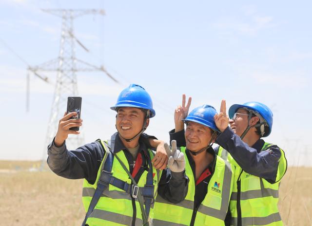 (250713) -- MINFENG, July 13, 2025 (Xinhua) -- Chen Lin (L) poses for a selfie with his colleagues after work at a construction site in Minfeng County, of Hotan Prefecture, northwest China's Xinjiang Uygur Autonomous Region, July 13, 2025. China has finished construction of a 4,197-km extra-high voltage power transmission loop around the Tarim Basin, home to the country's largest desert, marking a major infrastructure milestone in southern Xinjiang Uygur Autonomous Region.
   The final section of the 750-kilovolt (kV) loop, now the country's largest of its kind, was connected on Sunday, capping a 15-year project involving nine substations and nearly 10,000 steel towers, according to a subsidiary of State Grid Xinjiang Electric Power Co., Ltd., which constructed the project.
   The transmission line passes through extreme terrain, from the shifting sands of the desert to the high altitudes of the Kunlun Mountains.
   Chen Lin arrived in March this year at the southern edge of the Taklimakan Desert, where he, side by side with over 40 colleagues, accomplished part of the transmission line construction work despite sandy gusts and scorching temperature. (Photo by Zhang Limin/Xinhua)
