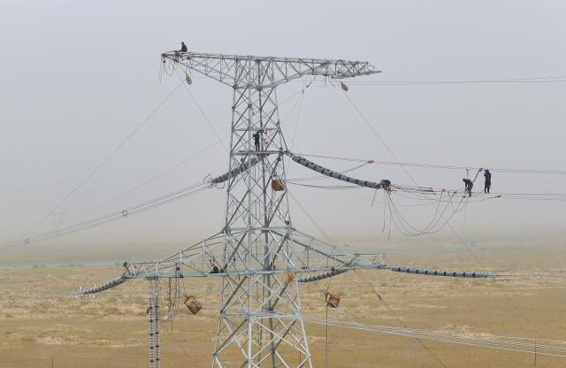(250713) -- MINFENG, July 13, 2025 (Xinhua) -- A drone photo shows Chen Lin (1st R) operating on a power transmission tower at a construction site in Minfeng County, of Hotan Prefecture, northwest China's Xinjiang Uygur Autonomous Region, July 12, 2025. China has finished construction of a 4,197-km extra-high voltage power transmission loop around the Tarim Basin, home to the country's largest desert, marking a major infrastructure milestone in southern Xinjiang Uygur Autonomous Region.
   The final section of the 750-kilovolt (kV) loop, now the country's largest of its kind, was connected on Sunday, capping a 15-year project involving nine substations and nearly 10,000 steel towers, according to a subsidiary of State Grid Xinjiang Electric Power Co., Ltd., which constructed the project.
   The transmission line passes through extreme terrain, from the shifting sands of the desert to the high altitudes of the Kunlun Mountains.
   Chen Lin arrived in March this year at the southern edge of the Taklimakan Desert, where he, side by side with over 40 colleagues, accomplished part of the transmission line construction work despite sandy gusts and scorching temperature. (Photo by Zhang Limin/Xinhua)