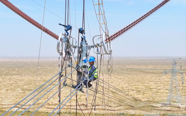 (250713) -- MINFENG, July 13, 2025 (Xinhua) -- A drone photo shows Chen Lin (R) operating at a construction site in Minfeng County, of Hotan Prefecture, northwest China's Xinjiang Uygur Autonomous Region, July 13, 2025. China has finished construction of a 4,197-km extra-high voltage power transmission loop around the Tarim Basin, home to the country's largest desert, marking a major infrastructure milestone in southern Xinjiang Uygur Autonomous Region.
   The final section of the 750-kilovolt (kV) loop, now the country's largest of its kind, was connected on Sunday, capping a 15-year project involving nine substations and nearly 10,000 steel towers, according to a subsidiary of State Grid Xinjiang Electric Power Co., Ltd., which constructed the project.
   The transmission line passes through extreme terrain, from the shifting sands of the desert to the high altitudes of the Kunlun Mountains.
   Chen Lin arrived in March this year at the southern edge of the Taklimakan Desert, where he, side by side with over 40 colleagues, accomplished part of the transmission line construction work despite sandy gusts and scorching temperature. (Photo by Zhang Limin/Xinhua)