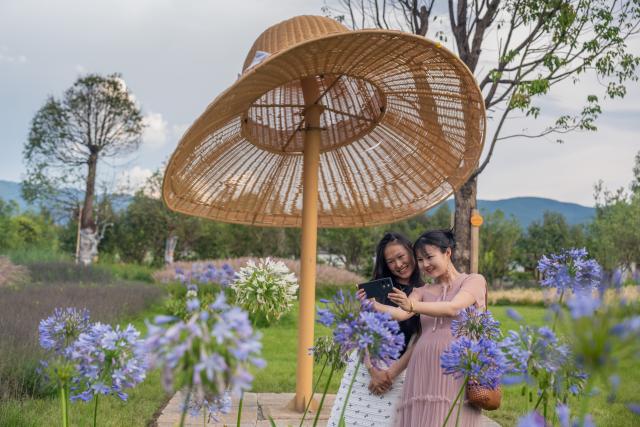 (250716) -- KUNMING, July 16, 2025 (Xinhua) -- Tourists pose for photos at a lakeside park in Dali Bai Autonomous Prefecture, southwest China's Yunnan Province, July 15, 2025. Known for its stunning nature beauty, Yunnan Province has cultivated a summer tourism industry, offering tourists diverse experiences amid forests, snow-capped mountains, wetlands, and flower fields. (Photo by Luo Xincai/Xinhua)