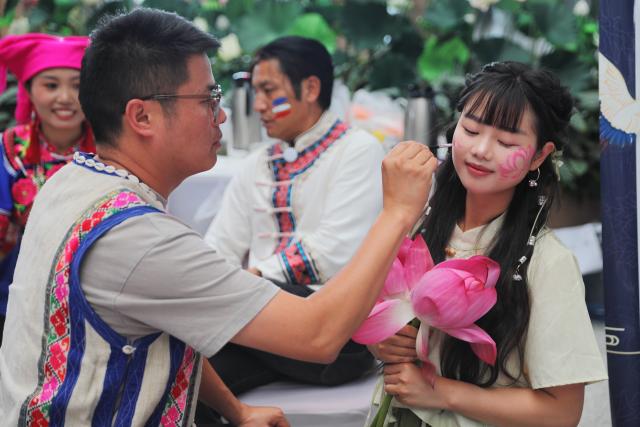 (250716) -- KUNMING, July 16, 2025 (Xinhua) -- A tourist experiences face daubing during an event celebrating Hualian ("daubed face") Festival at the departure hall of Kunming South Railway Station in Kunming, southwest China's Yunnan Province, July 14, 2025. Known for its stunning nature beauty, Yunnan Province has cultivated a summer tourism industry, offering tourists diverse experiences amid forests, snow-capped mountains, wetlands, and flower fields. (Photo by Yang Zixuan/Xinhua)