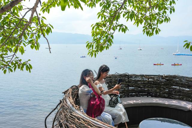 (250717) -- YUXI, July 17, 2025 (Xinhua) -- Tourists take a rest at a coffee shop by Fuxian Lake in Yuxi City, southwest China's Yunnan Province The beautiful scenery of Fuxian Lake in summer has attracted tourists nationwide. (Xinhua/Chen Xinbo)