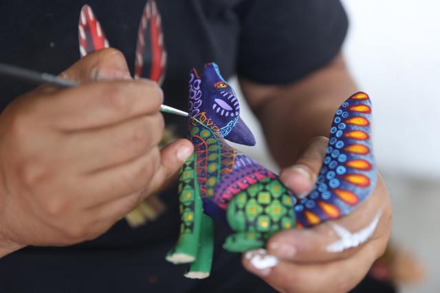 (250918) -- OAXACA, Sept. 18, 2025 (Xinhua) -- An artisan paints on a wood carving at a workshop in San Antonio Arrazola, Oaxaca State, Mexico, on Sept. 16, 2025. The village of San Antonio Arrazola on the outskirts of Oaxaca City is renowned for its colorful wood carvings. The process of making a wood carving includes chopping out shapes from the wood, carving, polishing, and applying hand-painted designs. These wood carvings often draw inspirations from animals, infused with fantasy and mythological elements. The craft is not only a signature local folk art but also a vital source of income for many local families. (Xinhua/Li Mengxin)