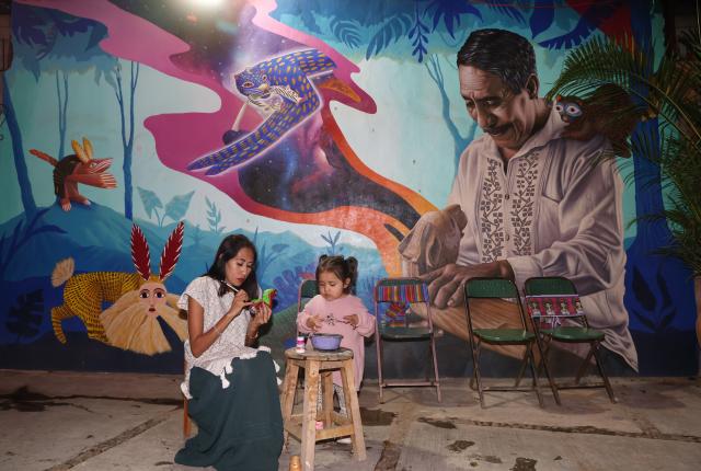 (250918) -- OAXACA, Sept. 18, 2025 (Xinhua) -- An artisan and his daughter paint on a wood carving at a workshop in San Antonio Arrazola, Oaxaca State, Mexico, on Sept. 16, 2025. The village of San Antonio Arrazola on the outskirts of Oaxaca City is renowned for its colorful wood carvings. The process of making a wood carving includes chopping out shapes from the wood, carving, polishing, and applying hand-painted designs. These wood carvings often draw inspirations from animals, infused with fantasy and mythological elements. The craft is not only a signature local folk art but also a vital source of income for many local families. (Xinhua/Li Mengxin)
