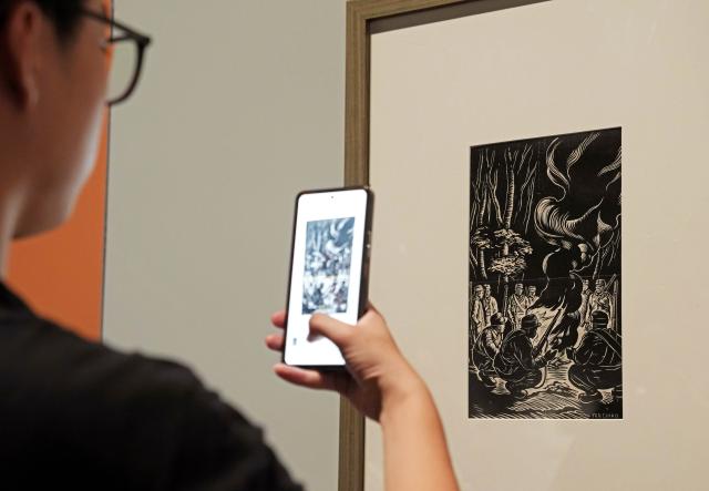 (250918) -- SHANGHAI, Sept. 18, 2025 (Xinhua) -- A visitor takes photos of a piece of work at a woodblock painting exhibition in commemoration of the 80th anniversary of the victory of the Chinese People's War of Resistance against Japanese Aggression and the World Anti-Fascist War in Shanghai, east China, Sept. 18, 2025. Kicking off Thursday at Shanghai Jiao Tong University, the exhibition showcases over 120 woodblock paintings. (Xinhua/Liu Ying)