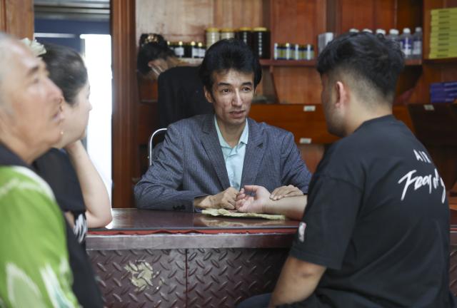 (250919) -- URUMQI, Sept. 19, 2025 (Xinhua) -- Metkasim Manglik (C) serves a customer at his herbal tea shop in Qira County, northwest China's Xinjiang Uygur Autonomous Region, Sept. 4, 2025.
  Hotan herbal tea has a long history and drinking tea has become an essential part of people's daily life here. It is made from more than 30 ingredients such as cloves, goji berries, ginger, dried tangerine peel, and roses, which are smashed before brewing. In 2021, the technique of making Hotan herbal tea was listed as a national-level intangible cultural heritage.
  Metkasim Manglik, one of the inheritors of Hotan herbal tea making, comes from a family that has been producing the tea since his grandfather. Starting at the age of 15, Metkasim began assisting his father in his family's business. Later, he studied at a local medical school and graduated in 2008. In 2019, Metkasim established his own company and created a product brand, categorizing and packaging Hotan herbal tea based on its health benefits.
  As an inheritor of the Hotan herbal tea making technique, Metkasim has had opportunities to participate in exhibitions and exchange programs in other regions. In places like east China's Anhui Province and southwest China's Sichuan Province, he has introduced his hometown's tea, receiving warm responses and even attracting interest from international visitors. The diverse local products and modern tea processing he encountered have given him more inspirations. "I'm excited that our Hotan herbal tea is gaining recognition, which motivates me even more to provide more tailored products for the customers," said Metkasim. (Xinhua/Wang Fei)