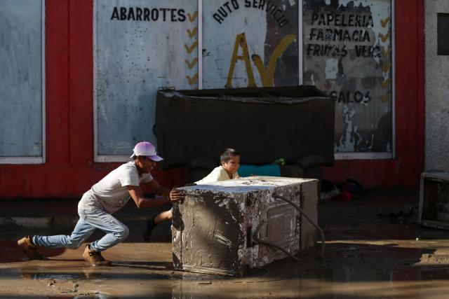(251013) -- POZA RICA(MEXICO), Oct. 13, 2025 (Xinhua) -- People push a washing machine through a street in the city of Poza Rica, Veracruz state, Mexico, Oct. 12, 2025. At least 64 people have died and dozens remain missing after days of torrential rains and flooding that hit central and eastern Mexico last week, authorities said Monday. (Photo by Francisco Canedo/Xinhua)