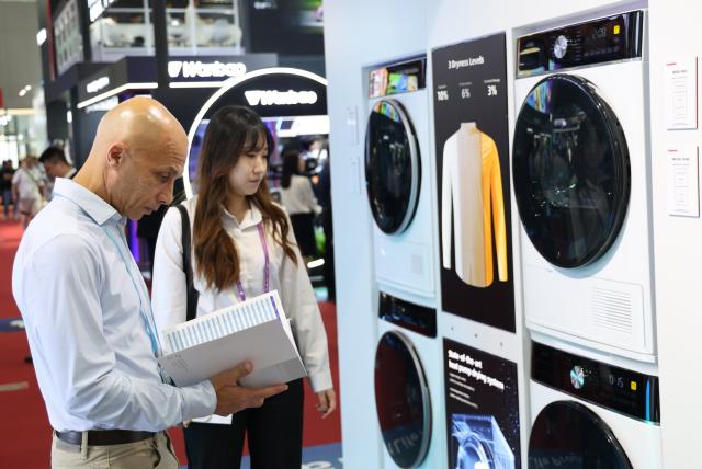 (251015) -- GUANGZHOU, Oct. 15, 2025 (Xinhua) -- A buyer (L) learns about washing machines during the 138th edition of the China Import and Export Fair in Guangzhou, south China's Guangdong Province, Oct. 15, 2025. The 138th edition of the China Import and Export Fair, also known as the Canton Fair, kicked off in Guangzhou on Wednesday, with the number of booths reaching 74,600 and exhibitors exceeding 32,000, both record high figures in the history of this famous event. (Xinhua/Lu Hanxin)