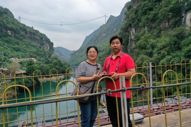 (251015) -- GUIYANG, Oct. 15, 2025 (Xinhua) -- This photo taken in November 2024 shows Xie Chaoqing, a local guesthouse owner, and his wife posing for a photo with the Huajiang Grand Canyon Bridge under construction in the background in southwest China's Guizhou Province. TO GO WITH "Across China: Beyond the steel span -- world's highest bridge uplifting China's mountainous southwest" (Xinhua)