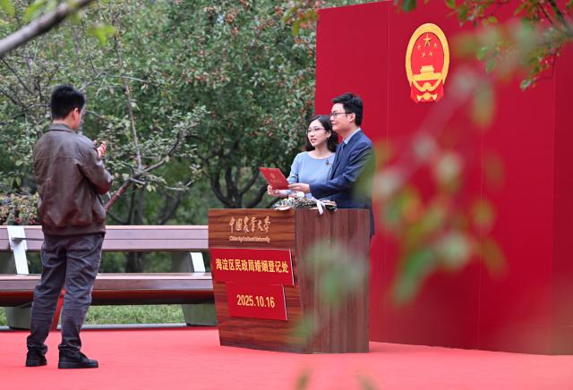 (251016) -- BEIJING, Oct. 16, 2025 (Xinhua) -- A couple pose for photos at a temporary marriage registration site at a campus of China Agricultural University in Beijing, capital of China, Oct. 16, 2025. The China Agricultural University on Thursday hosted a series of events to mark the 120th anniversary of its founding. (Xinhua/Chen Zhonghao)