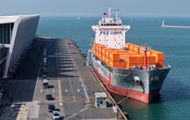 (251016) -- QINGDAO, Oct. 16, 2025 (Xinhua) -- A drone photo taken on Oct. 16, 2025 shows the "SMC RIZHAO" ship performing the maiden voyage of the Qingdao-Jeju container shipping route berthing at the Qingdao International Cruise Terminal in Qingdao, east China's Shandong Province. A regular direct container shipping route between Qingdao and South Korea's Jeju was launched on Thursday. This express shipping route will operate once a week in its initial stage, significantly enhancing the logistics efficiency between the two places, effectively reducing logistics costs, and further densifying the shipping network of east China's Shandong Province to South Korea. (Xinhua/Li Ziheng)