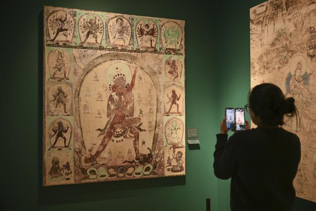 (251022) -- SHANGHAI, Oct. 22, 2025 (Xinhua) -- A guest takes photos of a Dunhuang mural during the preview of the Dunhuang Culture and Art Public Benefit Exhibition in east China's Shanghai, Oct. 22, 2025. The exhibition will kick off here on Oct. 23, and will last until March 31, 2026. (Xinhua/Chen Haoming)