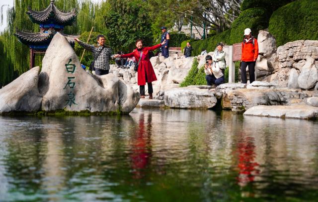(251022) -- JINAN, Oct. 22, 2025 (Xinhua) -- People enjoy their leisure time beside Baishi Spring in Jinan, east China's Shandong Province, Oct. 22, 2025. Many citizens and tourists here have recently been attracted by spouting springs along the city's spring greenway, a 6.6-kilometer-long pavement connecting several springs and historical sites along the city's moat and Daming Lake Park. (Xinhua/Xu Suhui)