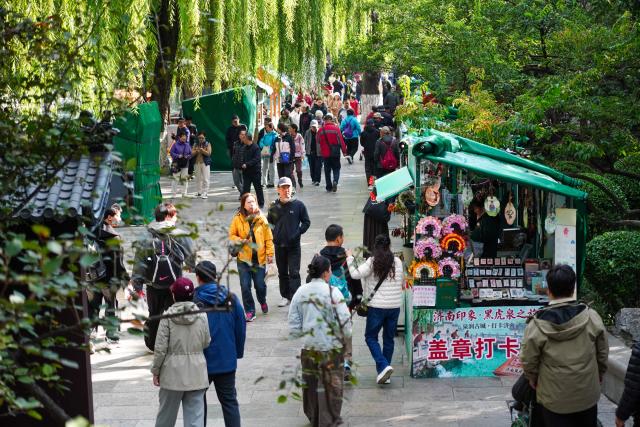 (251022) -- JINAN, Oct. 22, 2025 (Xinhua) -- People walk along the spring greenway in Jinan, east China's Shandong Province, Oct. 22, 2025. Many citizens and tourists here have recently been attracted by spouting springs along the city's spring greenway, a 6.6-kilometer-long pavement connecting several springs and historical sites along the city's moat and Daming Lake Park. (Xinhua/Xu Suhui)