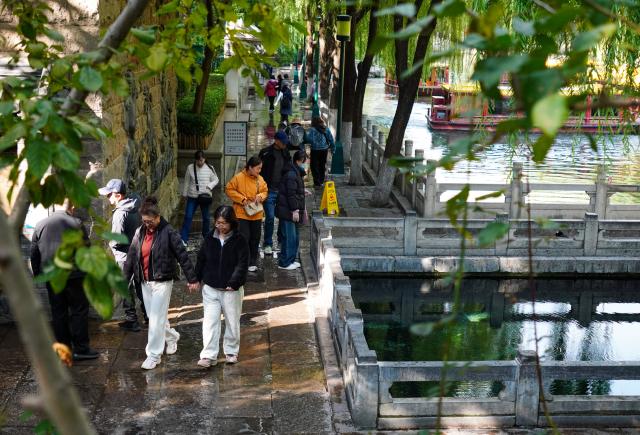 (251022) -- JINAN, Oct. 22, 2025 (Xinhua) -- People walk along the spring greenway in Jinan, east China's Shandong Province, Oct. 22, 2025. Many citizens and tourists here have recently been attracted by spouting springs along the city's spring greenway, a 6.6-kilometer-long pavement connecting several springs and historical sites along the city's moat and Daming Lake Park. (Xinhua/Xu Suhui)
