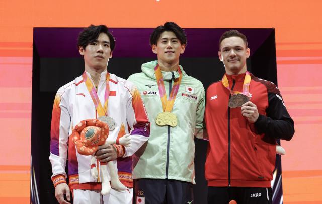 (251022) -- JAKARTA, Oct. 22, 2025 (Xinhua) -- Gold medalist Hashimoto Daiki (C) of Japan, silver medalist Zhang Boheng (L) of China and bronze medalist Noe Seifert of Switzerland pose for photos during the awarding ceremony for Men's All-Round at the 53rd FIG Artistic Gymnastics World Championships in Jakarta, Indonesia, on Oct. 22, 2025. (Xinhua/Bai Xuefei)