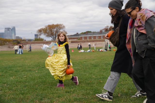 (251026) -- NEW YORK, Oct. 26, 2025 (Xinhua) -- A girl holding a pumpkin walks on a lawn at the Governors Island in New York, the United States, on Oct. 25, 2025.
  A festival was held at the Governors Island in New York on Saturday, attracting locals and visitors to celebrate the fall harvest with various family-friendly activities. (Xinhua/Zhang Fengguo)