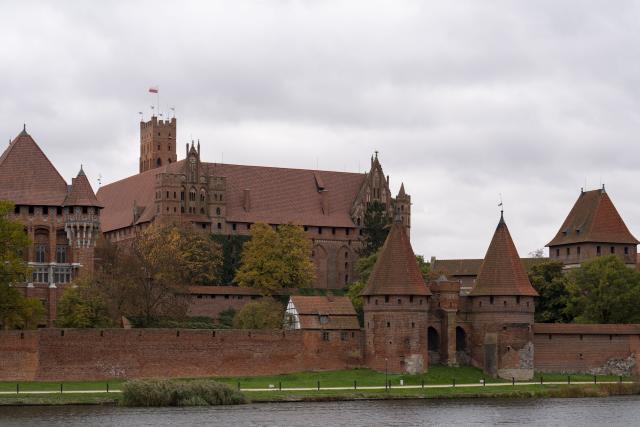 (251028) -- MALBORK, Oct. 28, 2025 (Xinhua) -- This photo taken on Oct. 27, 2025 from across the Nogat River shows a view of the Malbork Castle in Malbork, Poland. The Malbork Castle, also known as the Castle of the Teutonic Order, was built by the Teutonic Knights in the 13th century. The red-brick fortress covers about 200,000 square meters, making it one of the world's largest brick castles and a masterpiece of medieval Gothic military architecture. It was inscribed on the UNESCO World Heritage List in 1997 for its outstanding cultural and architectural value. (Xinhua/Xia Yuanyi)