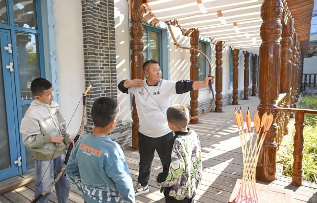 (251031) -- QAPQAL, Oct. 31, 2025 (Xinhua) -- Wu Junliang is a 37-year-old archer from Qapqal Xibe Autonomous County, a border county in northwest China's Xinjiang Uygur Autonomous Region - also proudly known as the hometown of Chinese archery. Wu is a recognized inheritor of the national intangible cultural heritage "Traditional Xibe Archery" and he has joined the "heritage-in-schools" initiative, offering free archery training to primary school students. He is called the "champion coach" by students.
Recognized for his strong arms and steady composure, Wu was admitted to a local archery school at the age of 16 to receive professional training. With outstanding talent, he quickly emerged, winning gold and silver medals in competitions at various levels. After retiring, he was hired as an archery coach for visitors at the Xibe Ancient Town.
For over a decade, Wu further studied traditional bows and taught himself multiple skills including horseback archery and rapid shooting at moving targets. As traditional bow competitions increased, he participated nationwide, winning multiple championships and training a number of apprentices. 
As intangible-heritage tourism gains popularity in recent years, Wu opened a 300-square-meter archery club in Yining City earlier this year, highlighting traditional bow culture. Wu Junliang (2nd R) repairs a traditional bow with several children around in his archery club in Yining City, northwest China's Xinjiang Uygur Autonomous Region, on Oct. 25, 2025. (Xinhua/Hu Huhu)