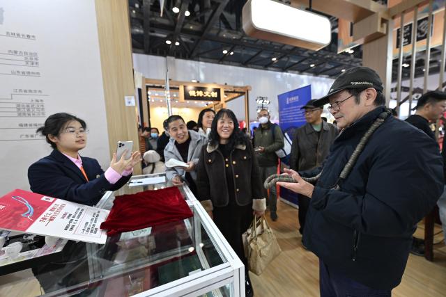 (251031) -- BEIJING, Oct. 31, 2025 (Xinhua) -- A visitor feels the weight of China's ancient coins during the Beijing International Coin Exposition 2025 at the China National Convention Center in Beijing, capital of China, Oct. 31, 2025. The three-day exposition kicked off here on Friday, attracting 323 exhibitors from 21 countries and regions. (Xinhua/Li Xin)