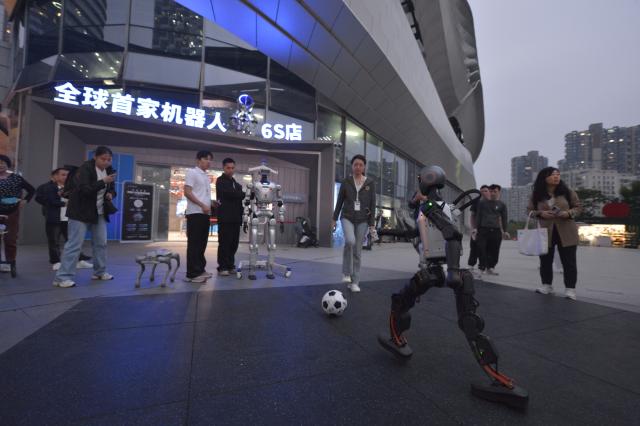 (251102) -- SHENZHEN, Nov. 2, 2025 (Xinhua) -- A humanoid robot plays football in front of a robot 6S store in Shenzhen, south China's Guangdong Province, Oct. 28, 2025. (Xinhua/Liu Lihang)